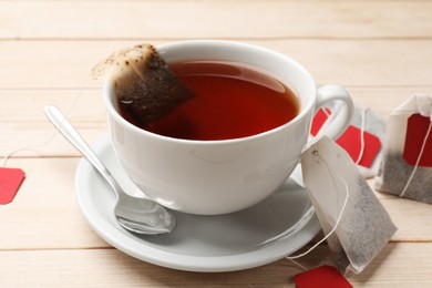 Photo of Tea bags, cup of hot beverage and spoon on light wooden table, closeup