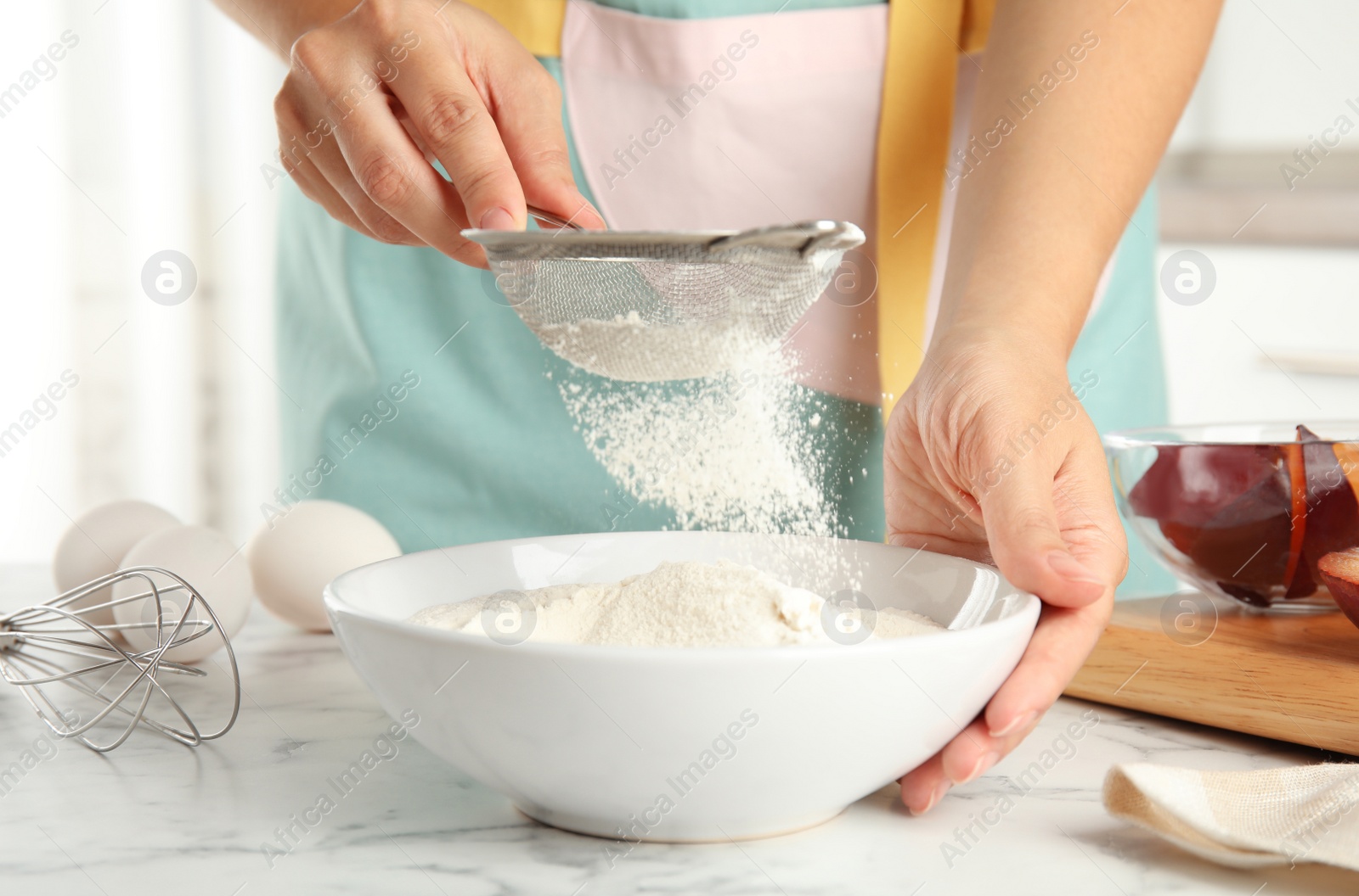 Photo of Woman sieving flour at white marble table, closeup. Cooking of delicious plum cake