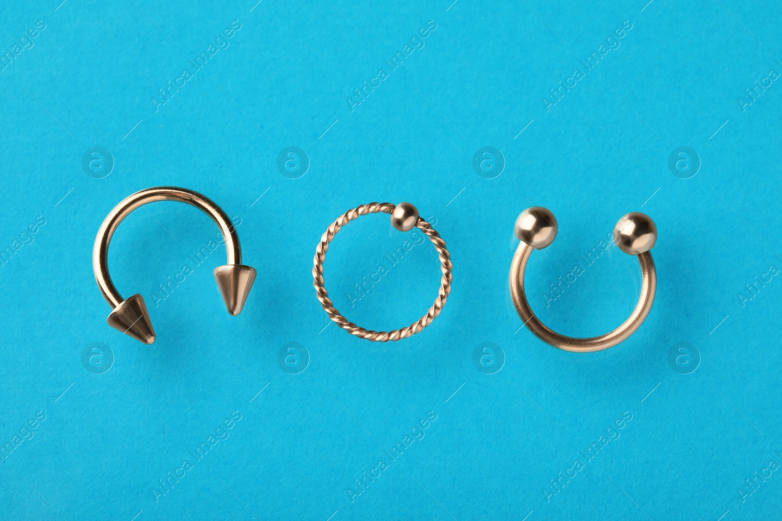 Photo of Different stylish rings for piercing on light blue background, flat lay