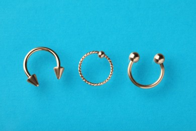 Photo of Different stylish rings for piercing on light blue background, flat lay