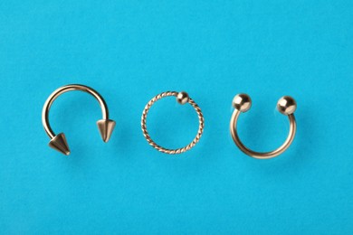 Different stylish rings for piercing on light blue background, flat lay