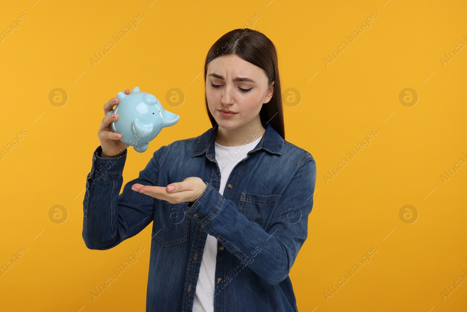 Photo of Sad woman with piggy bank on orange background