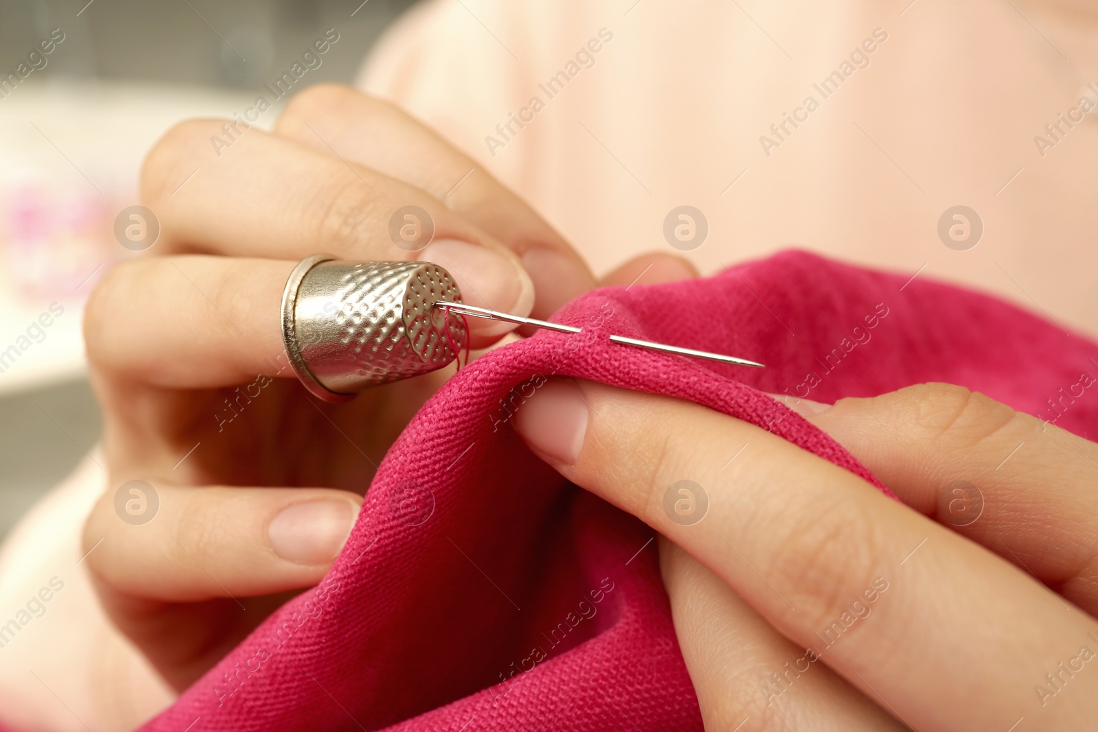 Photo of Woman sewing on red fabric with thimble and needle, closeup