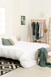 Photo of Wooden rack with clothes in modern bedroom interior