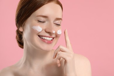 Photo of Smiling woman with freckles and cream on her face against pink background