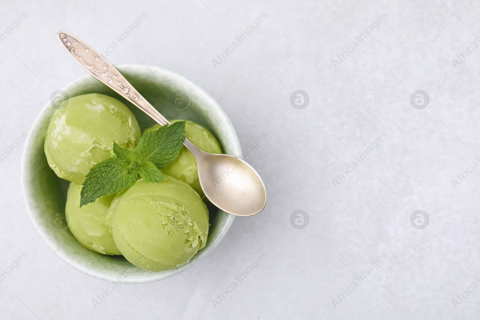 Photo of Tasty matcha ice cream and spoon in bowl on light grey table, top view. Space for text