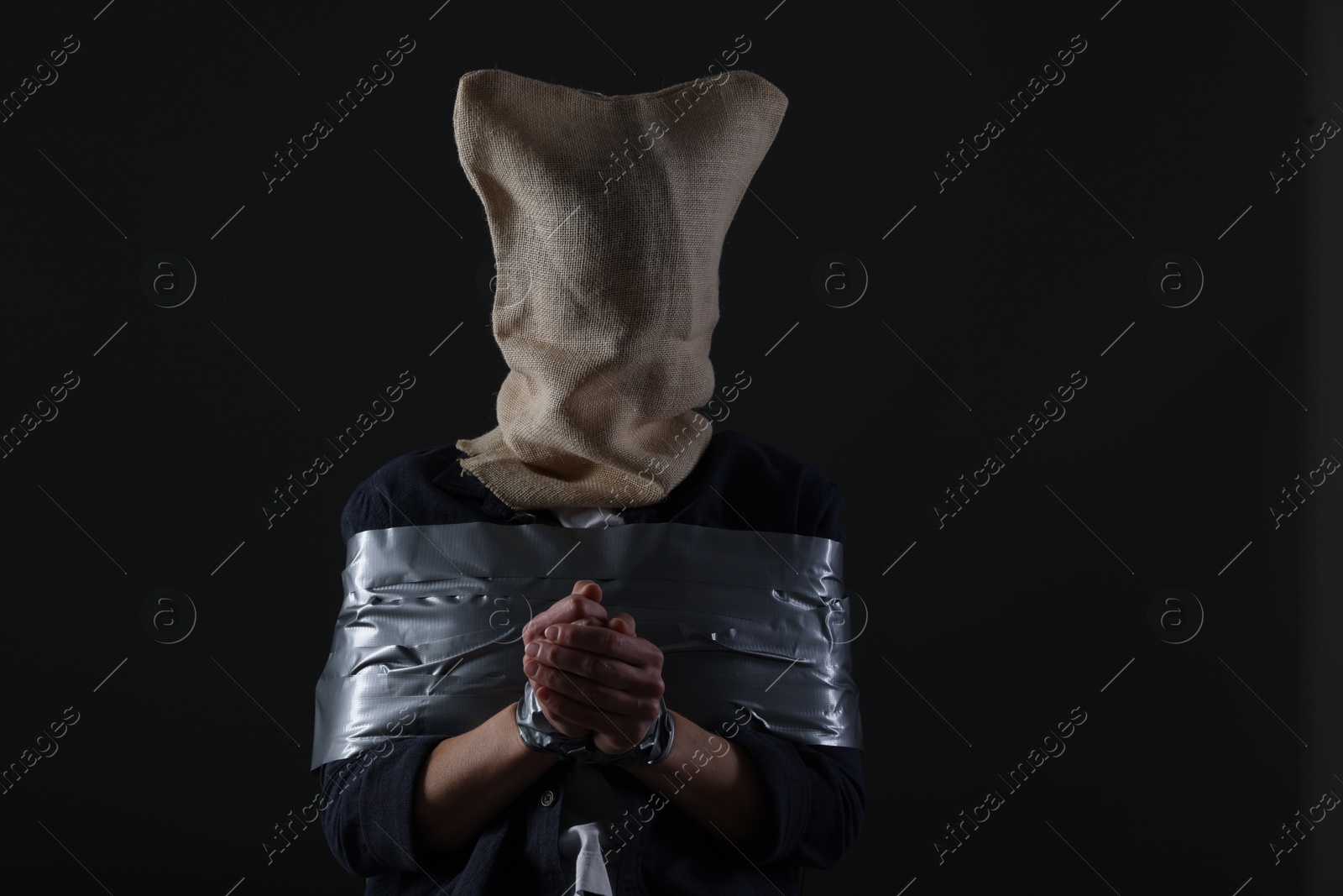 Photo of Taped up woman with bag on her head on dark background. Hostage