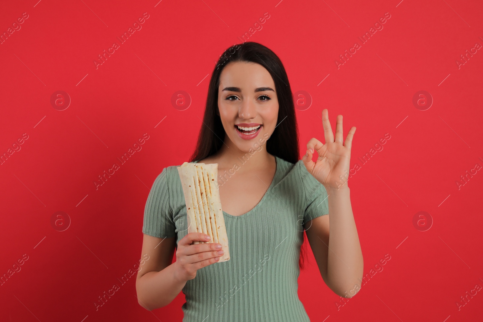 Photo of Happy young woman with tasty shawarma showing okay gesture on red background