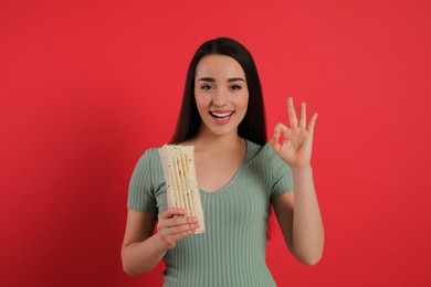 Happy young woman with tasty shawarma showing okay gesture on red background