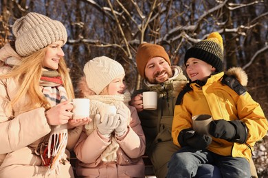 Happy family warming themselves with hot tea outdoors on snowy day