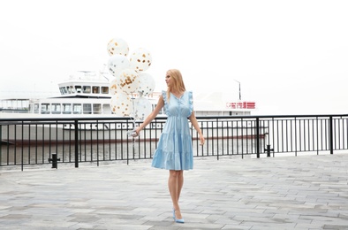 Photo of Beautiful young woman with bunch of balloons outdoors