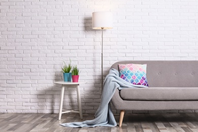 Photo of Cozy living room interior with sofa, pillow and plaid near brick wall. Space for text