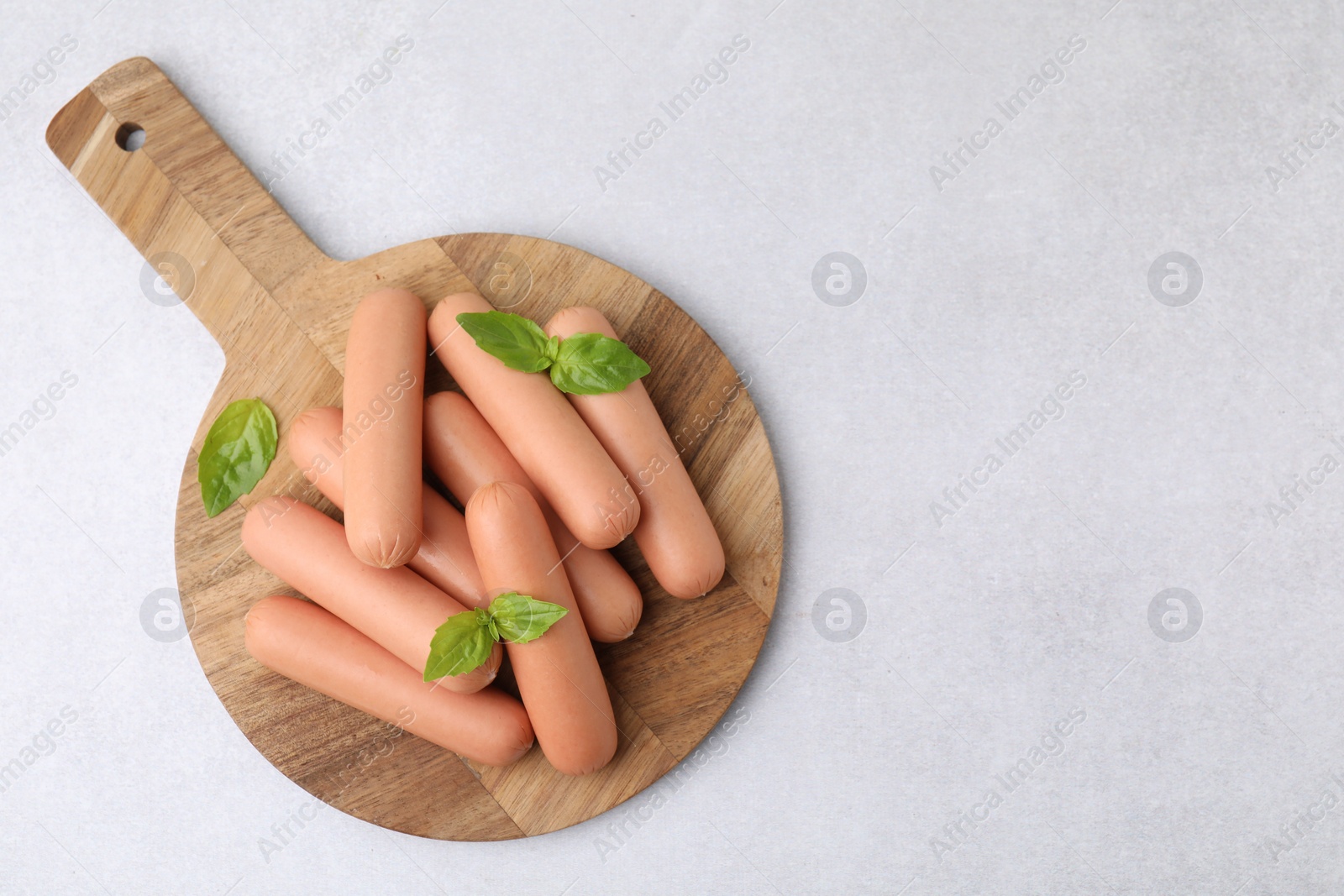 Photo of Delicious boiled sausages and basil on light gray table, top view. Space for text