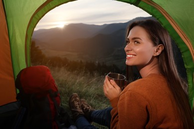 Young woman with drink inside of camping tent in mountains