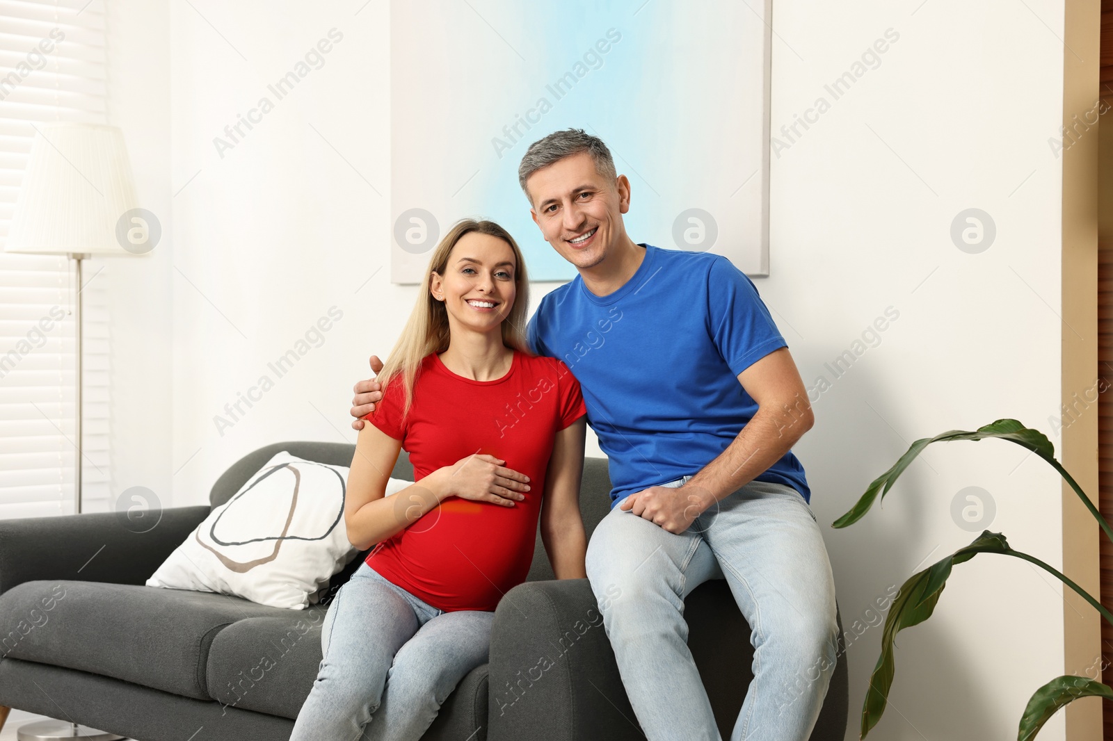 Photo of Young family housing concept. Pregnant woman with her husband on sofa at home