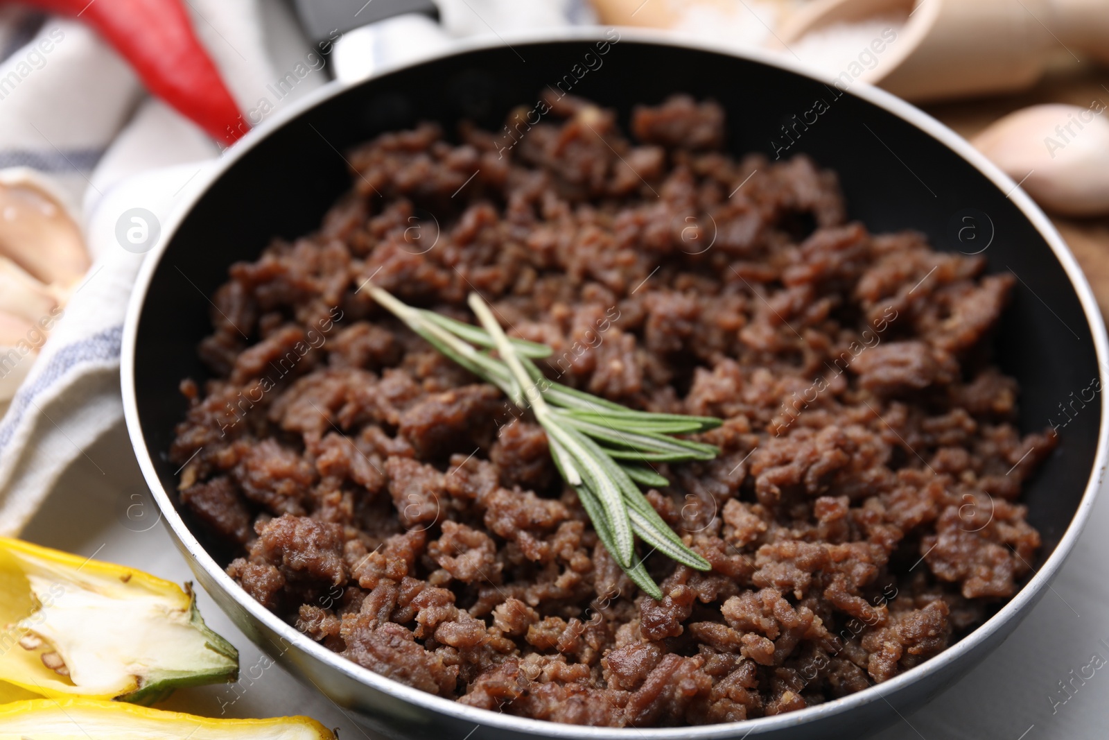 Photo of Fried ground meat in frying pan and rosemary on white table, closeup