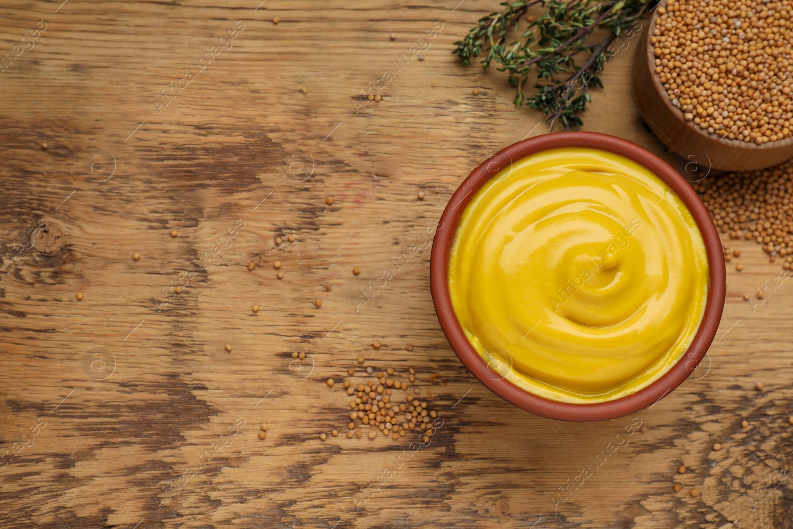 Photo of Delicious mustard, seeds and thyme on wooden table, flat lay. Space for text