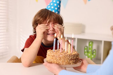 Photo of Birthday celebration. Mother holding tasty cake with burning candles near her son indoors