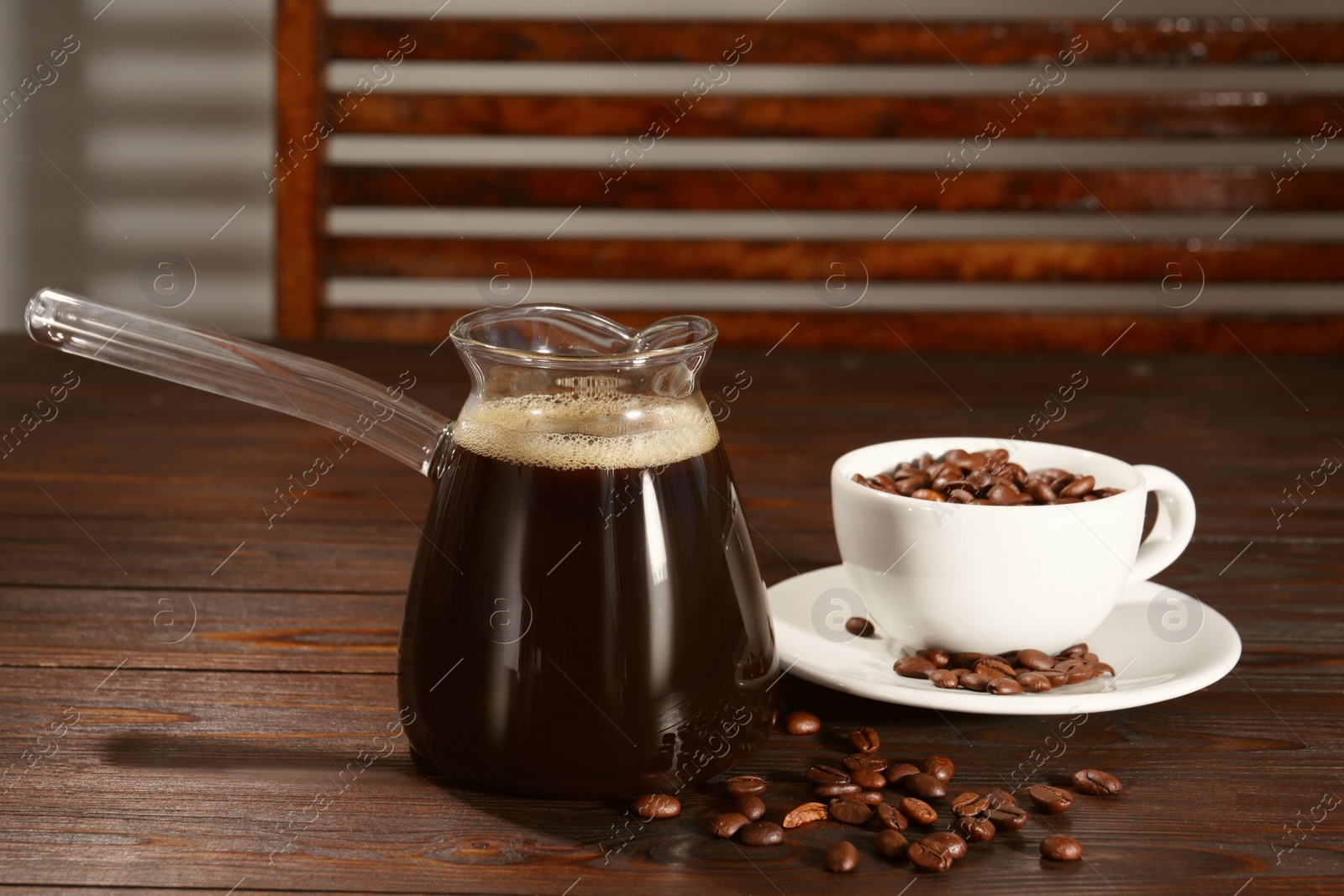 Photo of Glass turkish coffee pot with hot drink and beans on wooden table