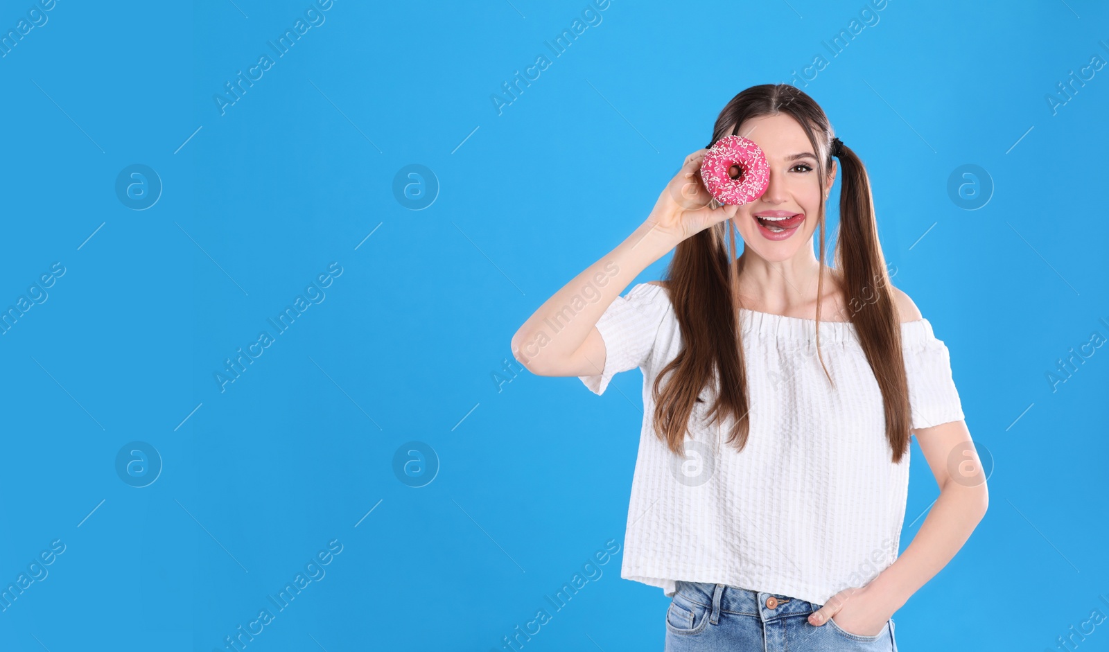 Photo of Beautiful young woman with donut on light blue background. Space for text