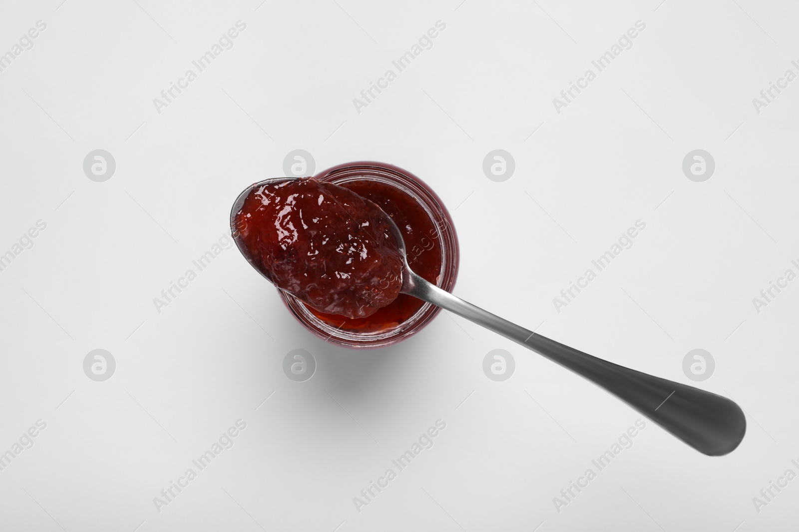 Photo of Spoon with tasty canned raspberry jam on jar against white background, top view