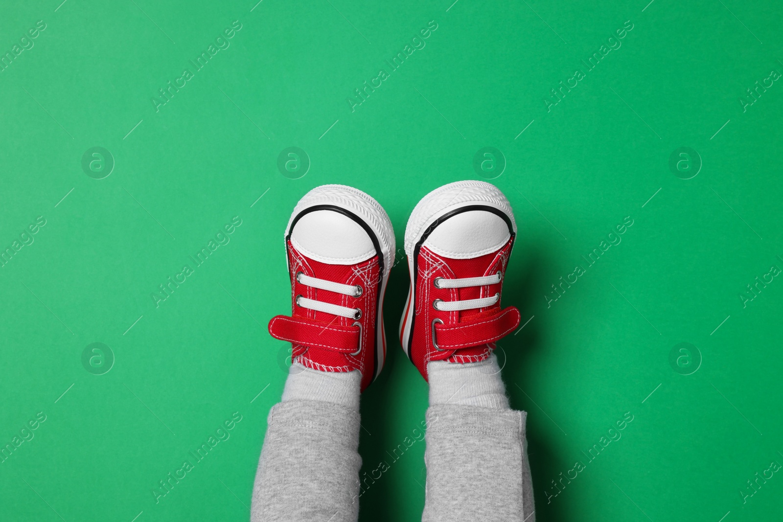 Photo of Little child in stylish red gumshoes on green background, top view