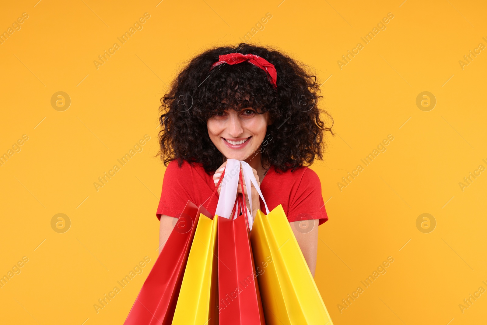 Photo of Happy young woman with shopping bags on yellow background