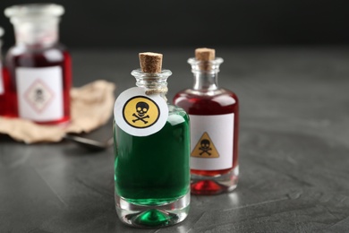 Photo of Glass bottles of poisons with warning signs on grey stone table
