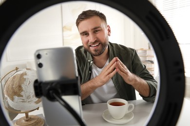 Photo of Blogger with cup of tea recording video at home, view through ring lamp