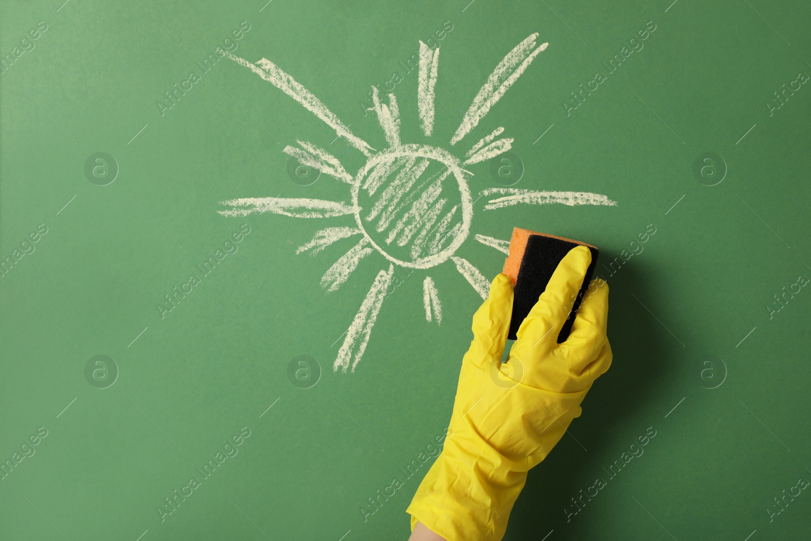 Photo of Woman erasing child's drawing from green wall, closeup