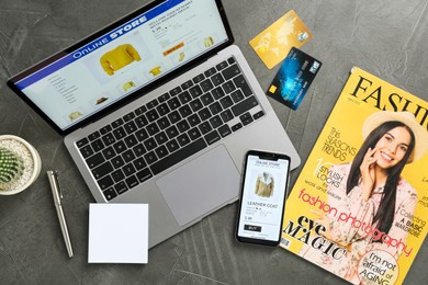 Photo of Online store website on laptop screen. Computer, smartphone, credit cards, stationery, magazine and cactus on grey table, flat lay
