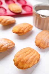 Delicious madeleine cookies and baking mold on white tiled table, closeup