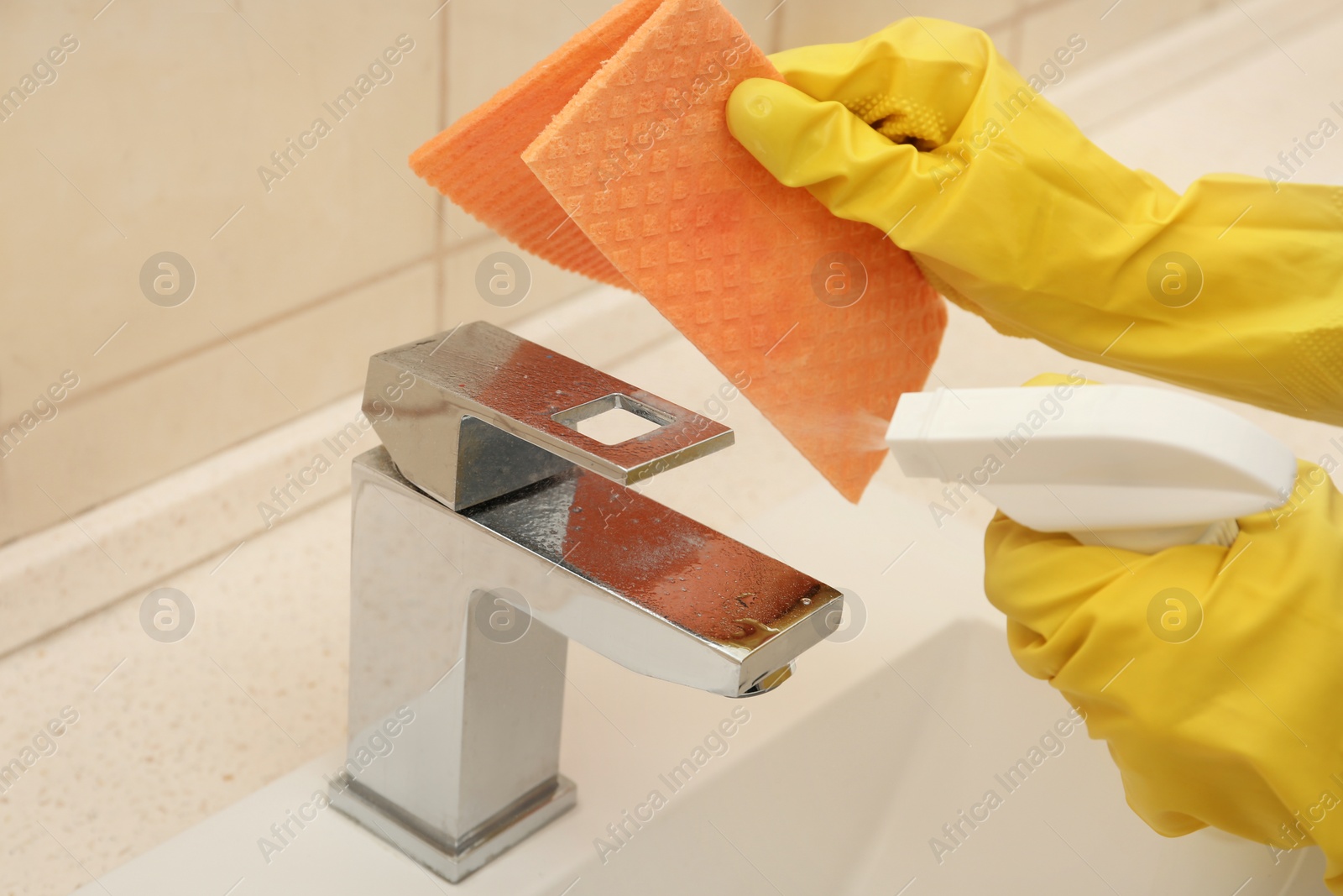 Photo of Person cleaning faucet with rag and detergent in bathroom, closeup