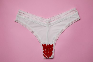 Photo of Woman's panties with red flower petals on pink background, top view