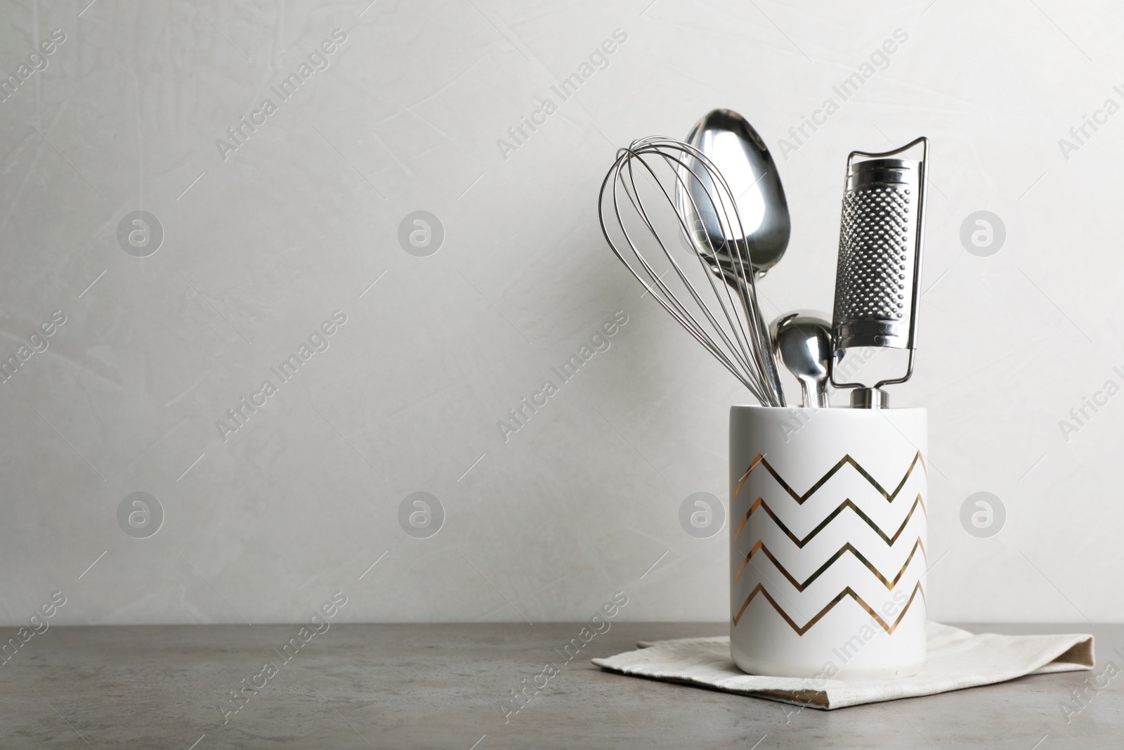 Photo of Holder with kitchen utensils and napkin on table. Space for text