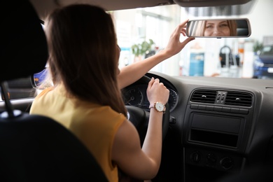 Photo of Young woman adjusting automobile rearview mirror