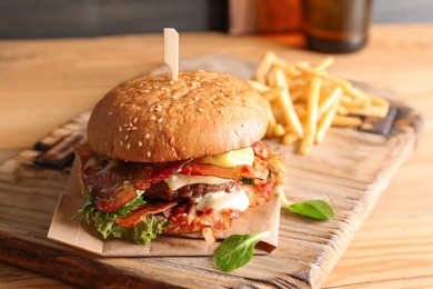 Tasty burger with bacon and french fries on wooden board