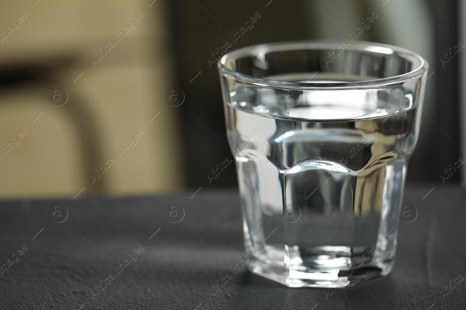 Photo of Glass of pure water on black table against blurred background, space for text