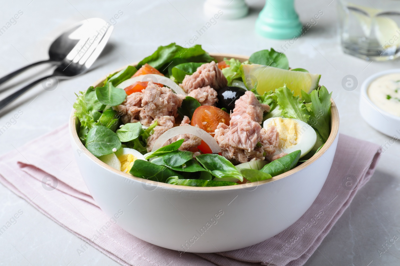 Photo of Bowl of delicious salad with canned tuna and vegetables on light table