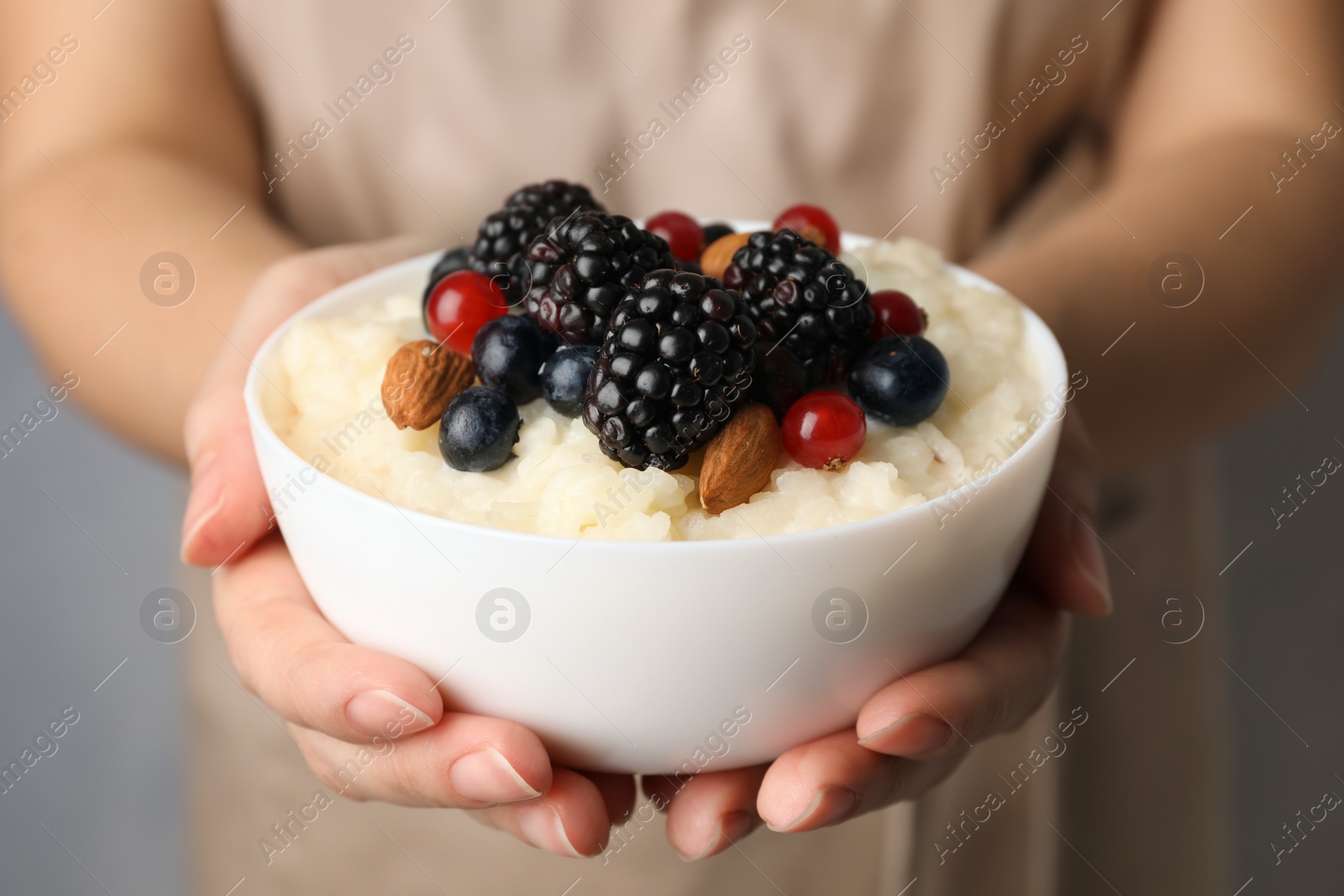 Photo of Woman holding bowl of delicious rice pudding with berries, closeup