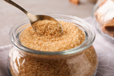 Taking spoon of brown sugar from glass bowl on table, closeup