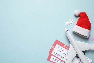 Photo of Santa hat, toy airplane and airline tickets on light blue background, space for text. Christmas vacation