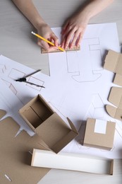 Woman creating packaging design at light wooden table, top view