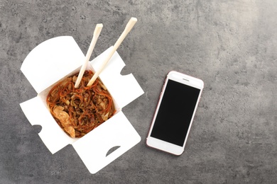 Photo of Smartphone with space for text and Chinese noodles on grey table, top view. Food delivery