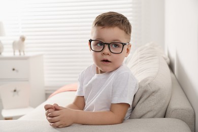 Cute little boy in glasses on sofa at home