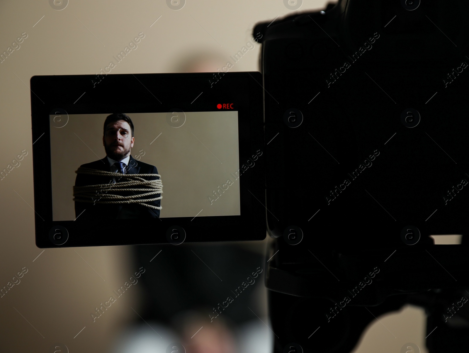 Photo of Man tied up and taken hostage on grey background, view through camera screen