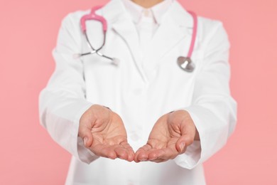 Photo of Doctor with stethoscope holding something on pink background, closeup