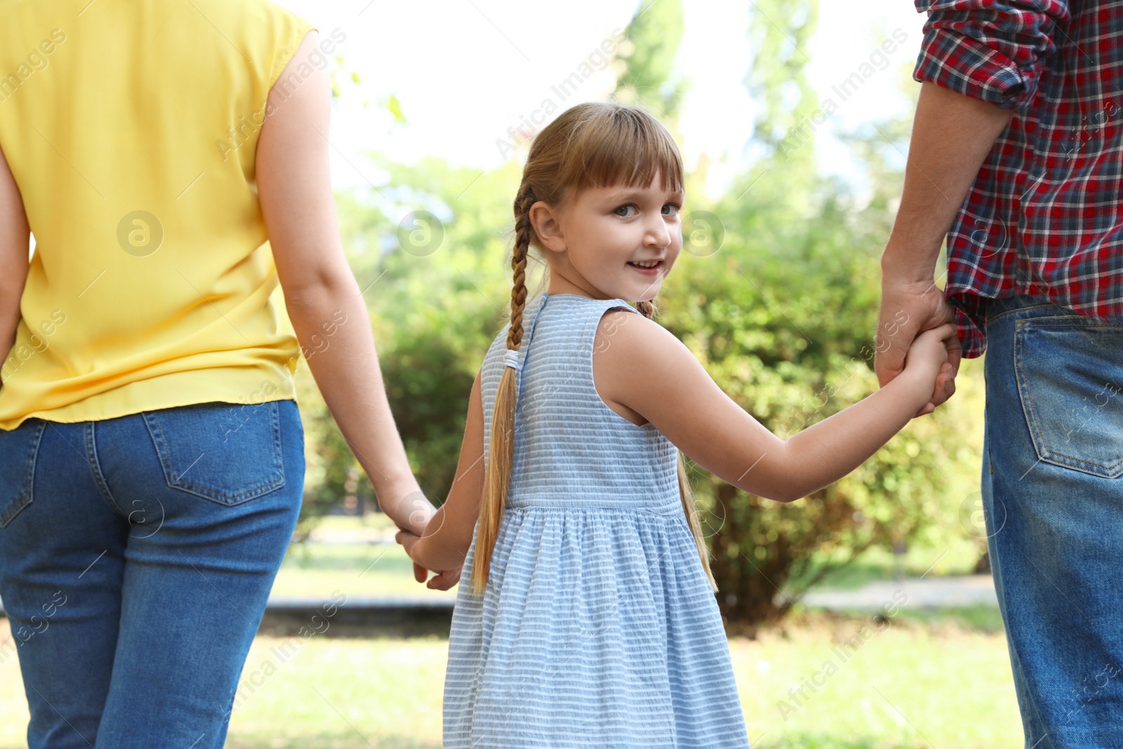 Photo of Little girl and her parents holding hands outdoors. Family weekend