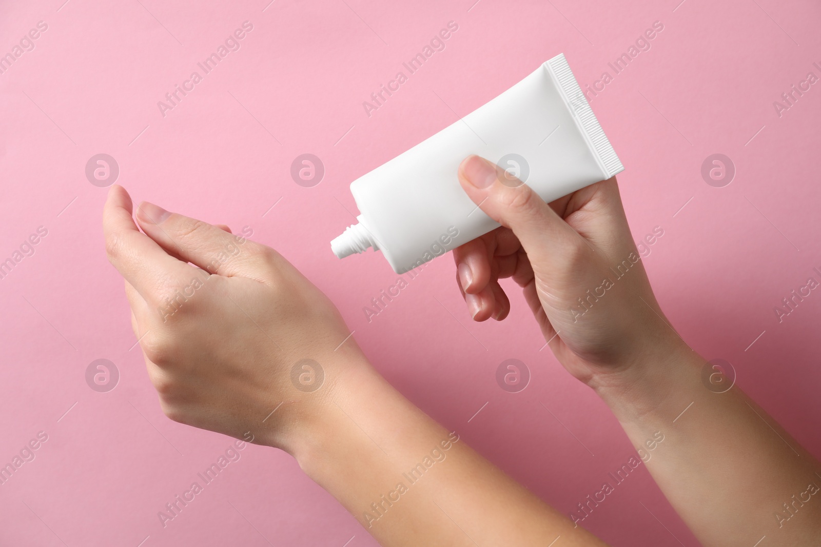 Photo of Woman applying cosmetic cream from tube onto her hand on pink background, closeup