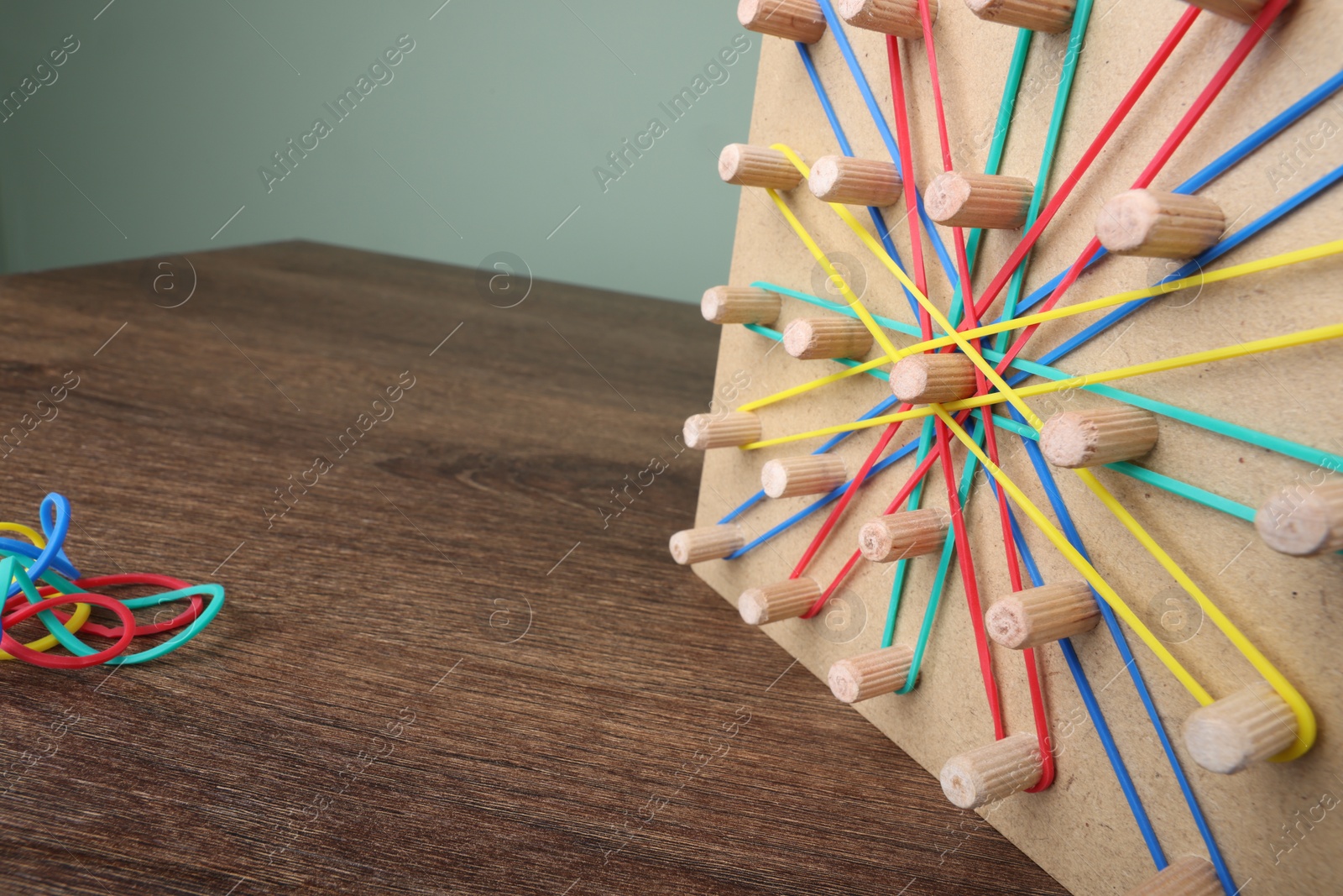 Photo of Wooden geoboard and rubber bands on table, closeup with space for text. Motor skills development